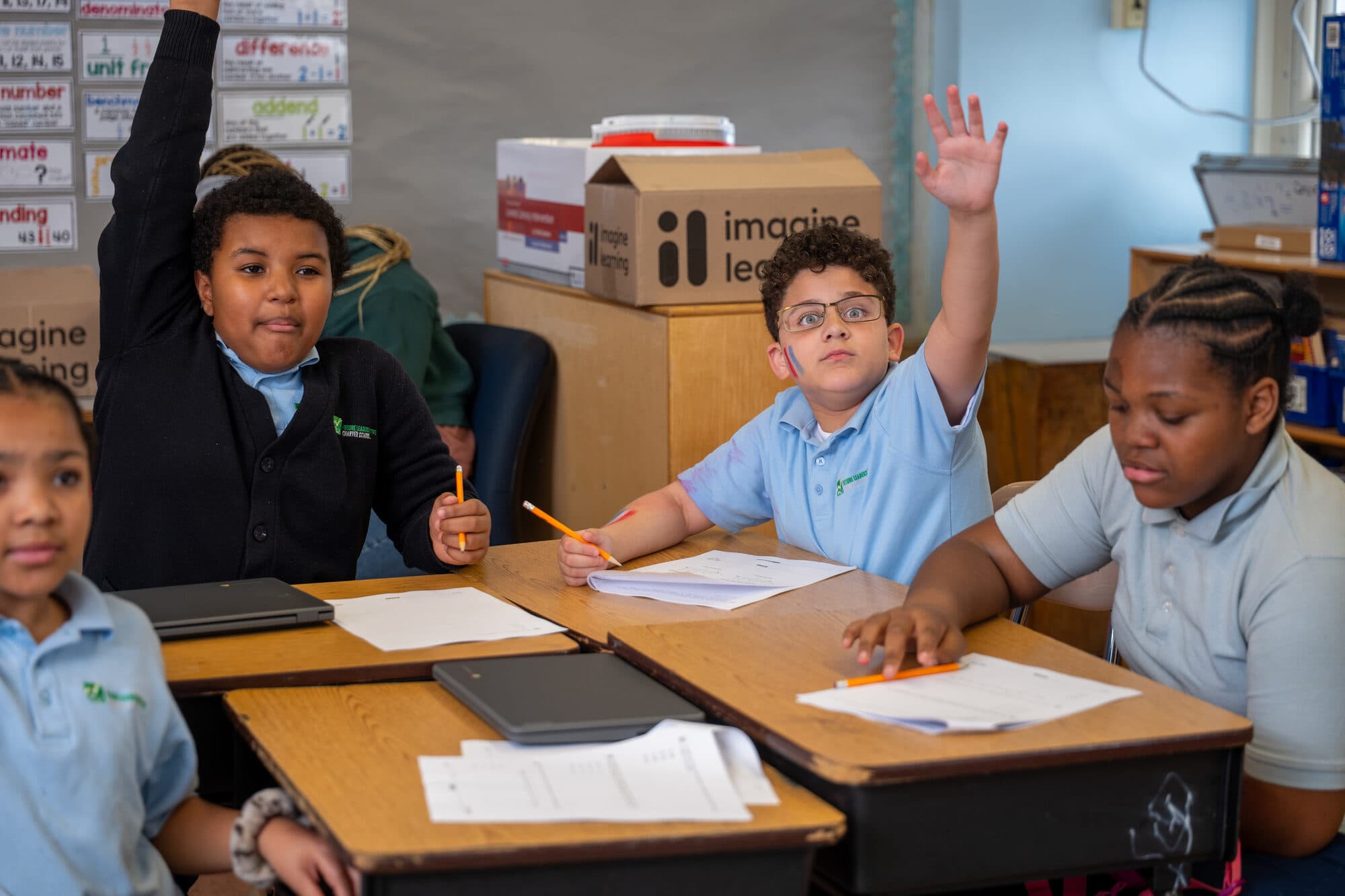 FLI students at work in class, hands raised.