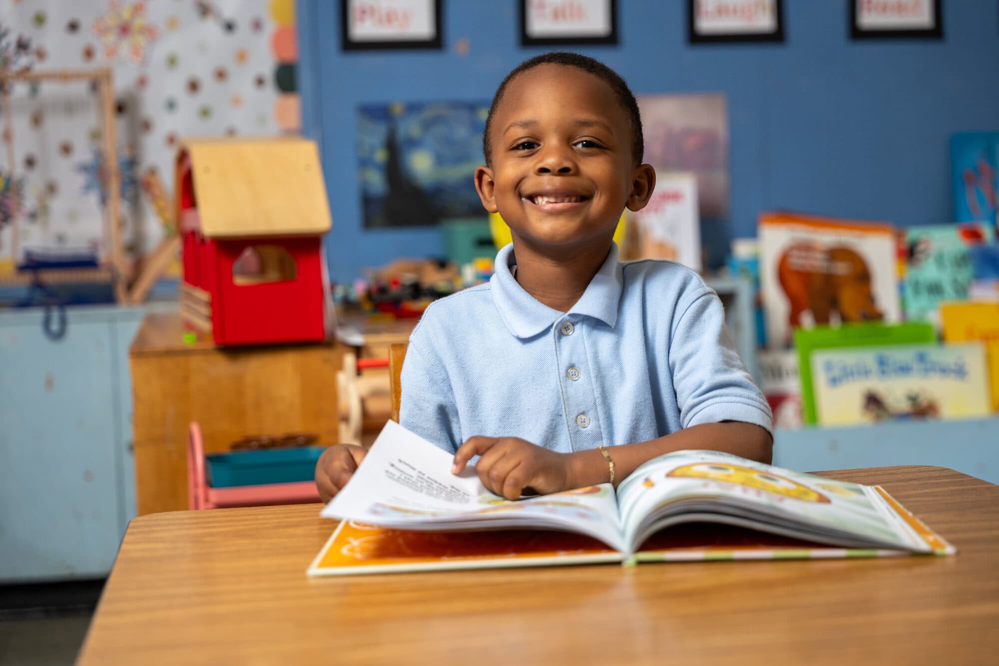 A young FLI student smiling over an open book at their desk.