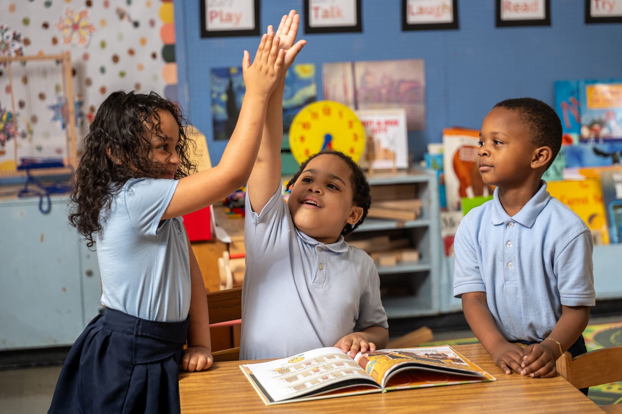 FLI students at work together in class, one with a hand raised.